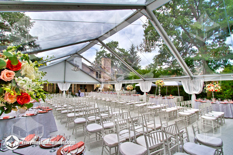 This 40x75 clear top wedding tent is all set for a ceremony, with ballroom chairs, white carpet, and plenty of floral decor.