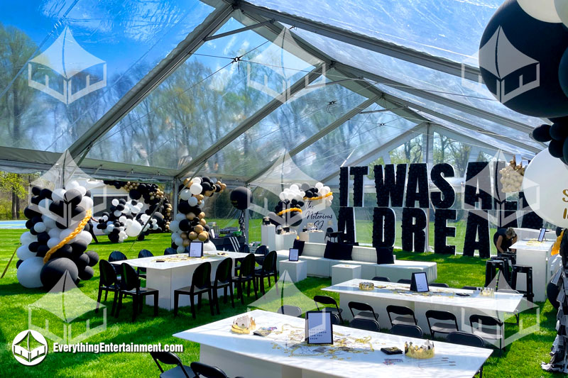 30x50 clear top tent with elegant black, white, and gold decor, featuring draped fabric, chandeliers, and a stylish dining setup for a luxury event.